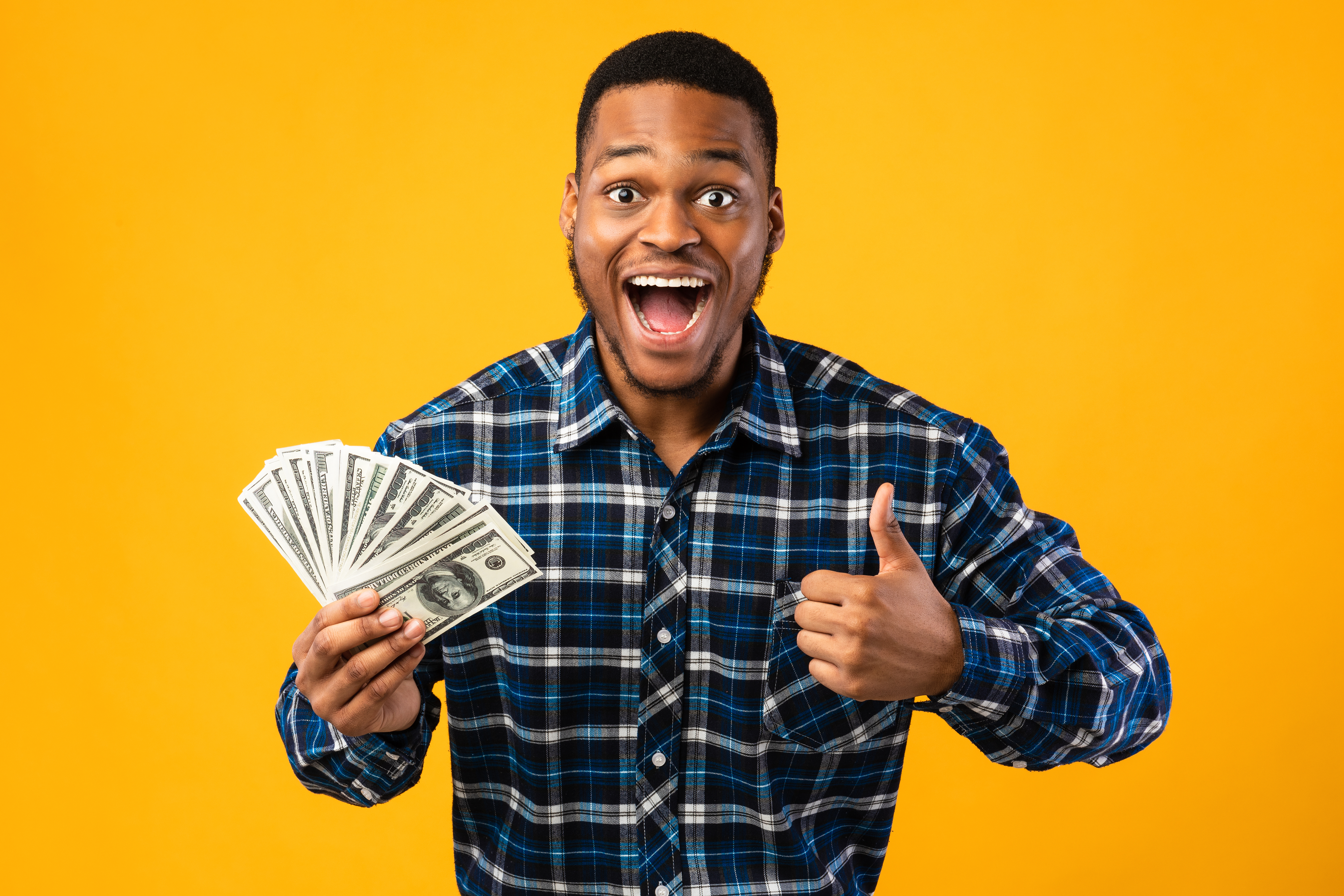 man smiling with cash in one hand, making thumbs-up gesture with the other